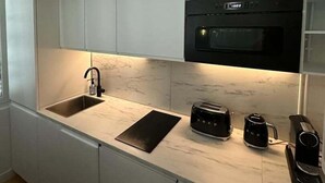 Una cocina moderna con armarios blancos, un horno negro, un lavamanos, un tostador y una cafetera.