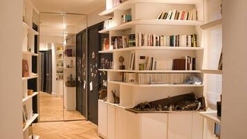 Ein schmaler Korridor mit weißen Regaleinheiten, gefüllt mit Büchern und Dekoration, der zu einer dunklen Tür führt.