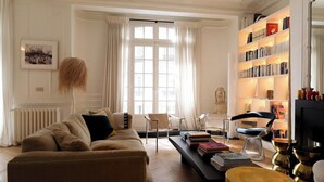 Een woonkamer met een bank, stoelen, een salontafel met boeken, een boekenkast en een open haard.