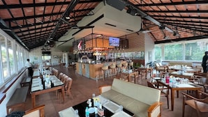Un ristorante spazioso con soffitti alti, un'area bar e diverse opzioni di posti a sedere, tra cui tavoli e un divano.