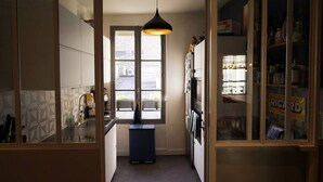 A narrow kitchen with a window, a hanging light fixture, and a refrigerator. - Beautiful apartment 4 ppl. / Pigalle - Montmartre (Paris)