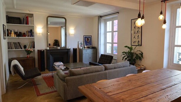 A living room with a wooden table, grey sofas, a bookshelf, and a fireplace. - Beautiful apartment 4 ppl. / Pigalle - Montmartre (Paris)