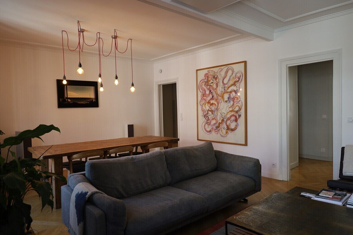 A living room with a gray sofa, a wooden dining table, and a large abstract painting on the wall.