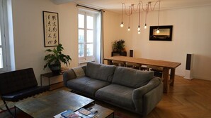A modern living room with a grey sofa, a coffee table with books, a dining table, and a potted plant. - Beautiful apartment 4 ppl. / Pigalle - Montmartre (Paris)