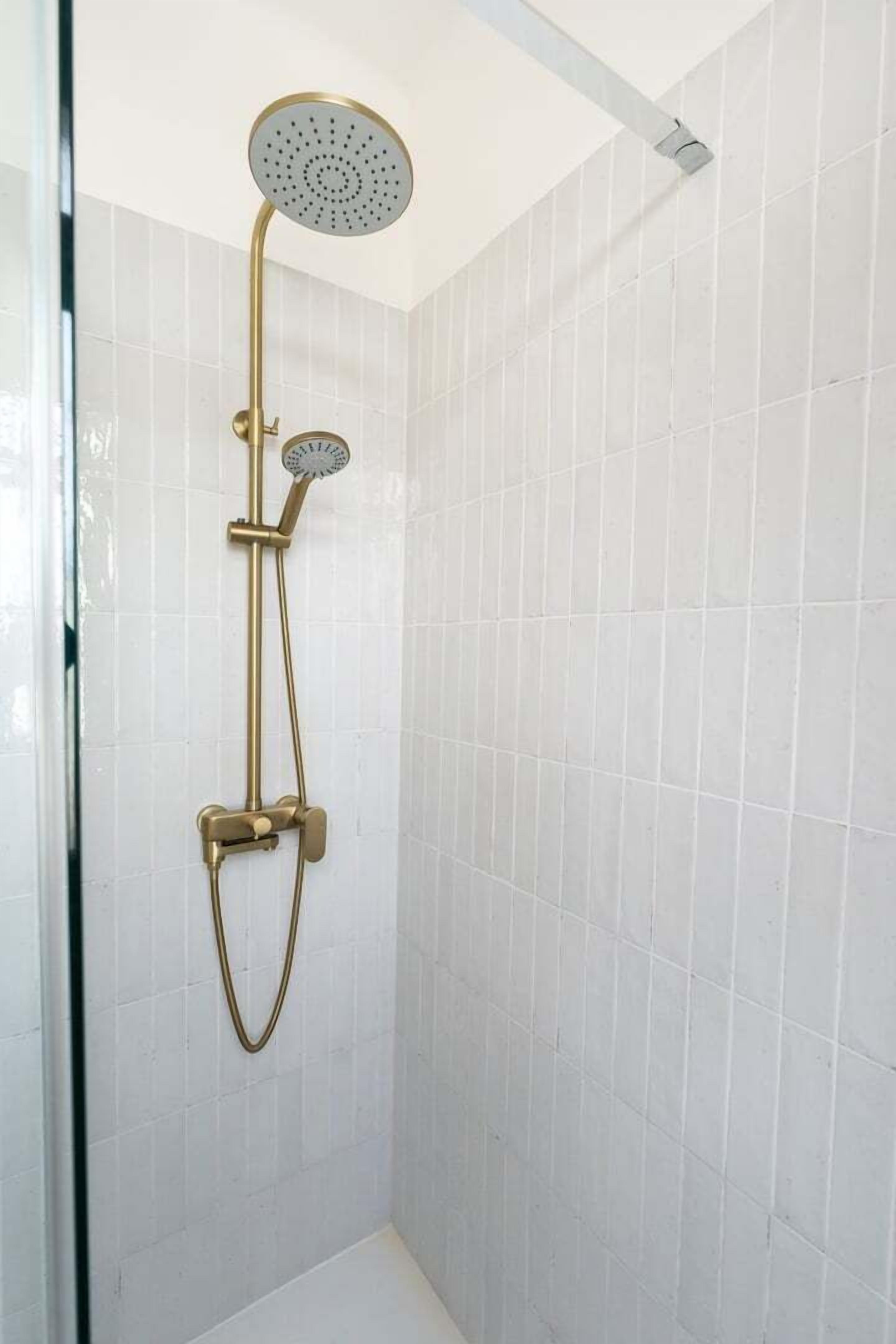 A shower with a handheld showerhead and a wall-mounted faucet in a tiled room.