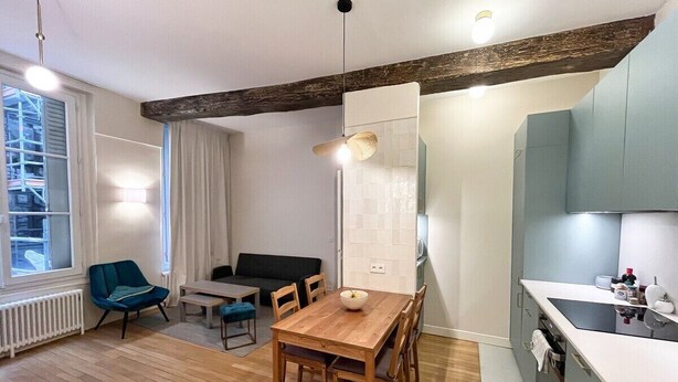 A modern kitchen with a wooden table and chairs, a built-in oven, and a window overlooking a cityscape. - Beautiful Renovated Apartment in Le Marais (Paris)