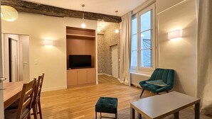 A modern living room with a wooden dining table, a green armchair, a TV, and a fireplace. - Beautiful Renovated Apartment in Le Marais (Paris)
