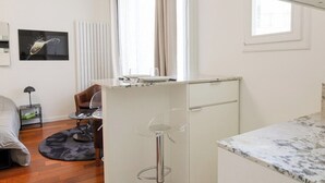 A compact kitchen with a marble countertop, a white refrigerator, and a dining area with a table and chairs. - New Studio at the Heart of Opera - Paris 1st (Paris)