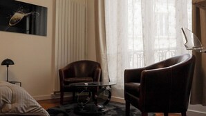 A room with a bed, a round table, two leather armchairs, a floor lamp, a radiator, and a window with sheer curtains. - New Studio at the Heart of Opera - Paris 1st (Paris)