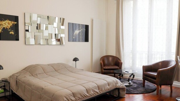 A modern bedroom with a bed, two chairs, a small table, and artwork on the walls. - New Studio at the Heart of Opera - Paris 1st (Paris)
