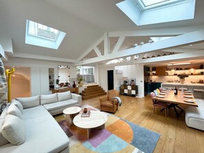 A spacious living room with a high ceiling, skylights, a dining area, and a kitchen.
