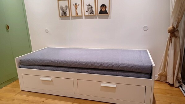 A bed with storage drawers and a grey mattress, a green door, and framed animal pictures on the wall.