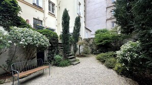 A gravel courtyard with a wooden bench, surrounded by greenery and buildings. - Spacious apartment in Batignolles (Paris)