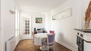 A dining area with a round table, purple chairs, a white tablecloth, a coffee machine, and a painting on the wall. - Spacious | in the Heart of the Marais | 4 people (Paris)