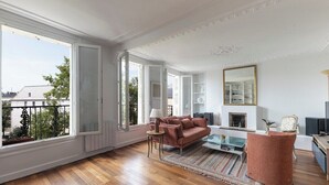 A spacious living room with a large window, a sofa, a coffee table, and a fireplace. - Spacious | in the Heart of the Marais | 4 people (Paris)