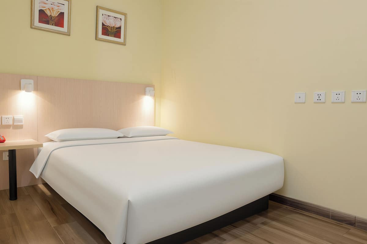 Quarto de hotel com cama, mesa de cabeceira, abajur e tomadas na parede.