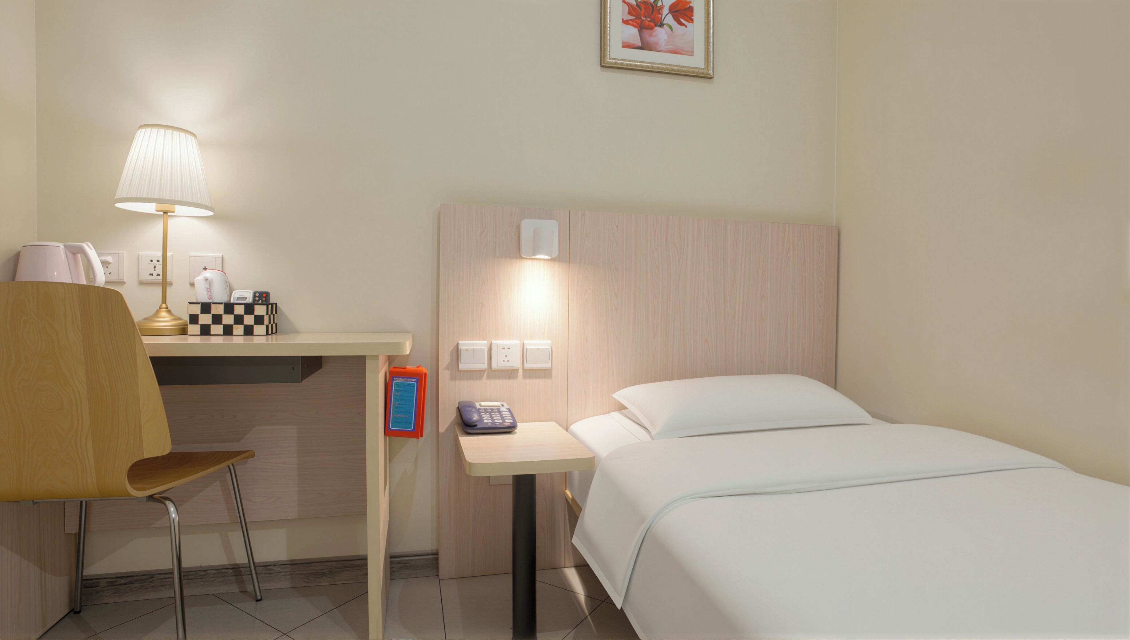 Habitación de hotel con cama, escritorio con lámpara, silla, teléfono y una mesita.