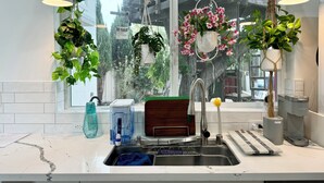Eine moderne Küche mit großem Fenster, hängenden Pflanzen, einem Wasserspender und einer Kaffeemaschine.