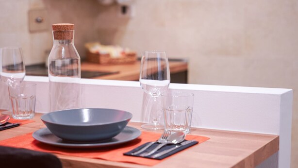 Mesa de comedor dispuesta con un tazón, vasos y cubiertos sobre una mesa de madera con un separador blanco.