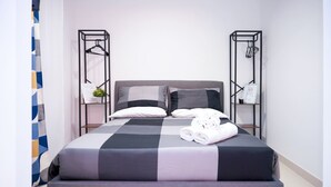 Una cama doble con colcha a cuadros, dos mesitas de noche con estructura de metal negro y un perchero de toallas en la pared a cada lado.