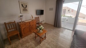 A room with a wooden cabinet, a television, a small table with a vase, and a chair. - Las Floritas 5 - Plumeria (Playa de Las Americas)