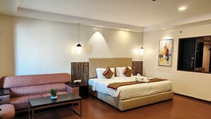 Una habitación de hotel moderna con un sofá, una cama con cabecera, una mesita de noche y una planta pequeña.
