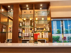 A bar area with multiple shelves of liquor bottles and glasses, a large glass of a red beverage, and a view of the outdoors through a window. - The Altruist Wagholi Hotel (Pune)