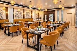 A restaurant with multiple tables and chairs, a herringbone floor pattern, and pendant lighting. - The Altruist Wagholi Hotel (Pune)
