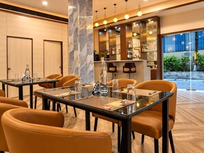 A hotel dining area with tables set for four, equipped with glassware and cutlery. - The Altruist Wagholi Hotel (Pune)