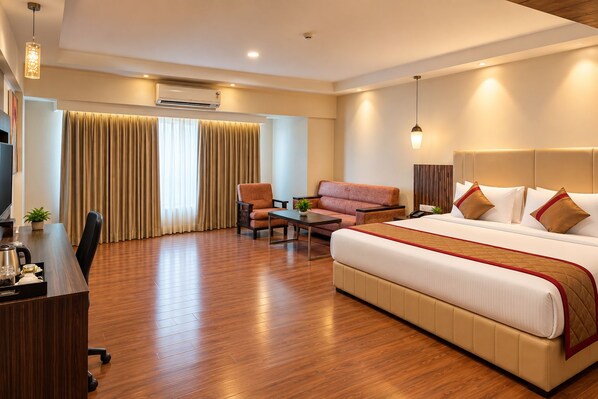 A hotel room with a bed, a desk, a chair, a sofa, and a coffee table. - The Altruist Wagholi Hotel (Pune)