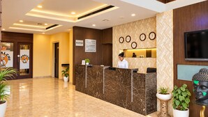 Zona de recepción de hotel con un mostrador de mármol, una recepcionista, un cartel de recepción, relojes de pared y una estatua de Buda.