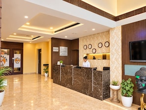 Et hotellets reception område med en marmorindtægt receptionsdisk, en receptionist, receptionsskilt, vægur og en Buddha statue.