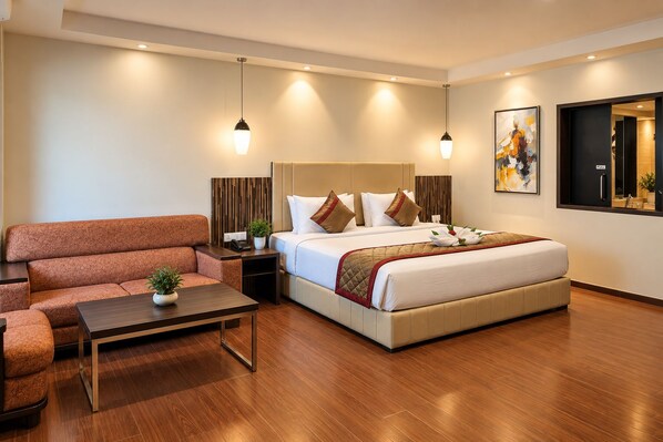 A hotel room with a bed, a sofa, a small table, and a nightstand. - The Altruist Wagholi Hotel (Pune)