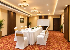 A conference room with a long table, white chairs, a whiteboard, and a large plant. - The Altruist Wagholi Hotel (Pune)