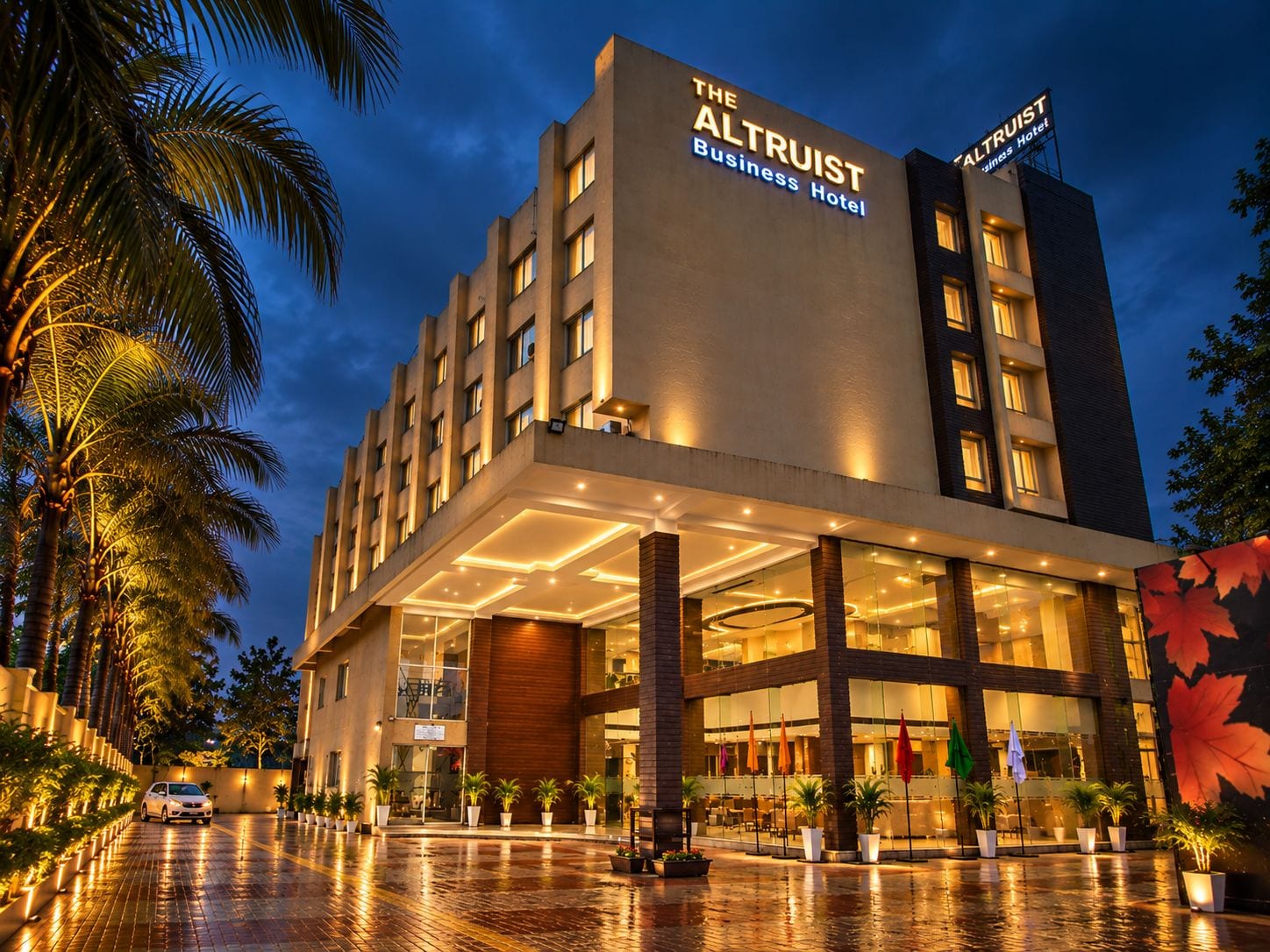 A modern hotel with a prominent sign, a covered entrance, and a wet ground, suggesting recent rain.