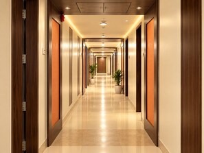 Un long couloir bien éclairé, avec des portes en bois et un sol carrelé, qui mène à plusieurs pièces.