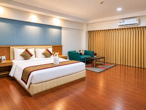 A hotel room with a bed, a sofa, a coffee table, and an air conditioning unit. - The Altruist Wagholi Hotel (Pune)