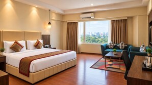 Habitación de hotel con una cama grande, un sofá, una mesita de centro y vistas a la ciudad a través de la ventana.