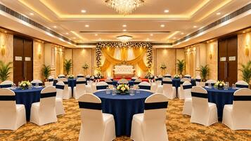 Un salón de banquetes con mesas redondas, sillas blancas y un escenario con decoraciones florales.