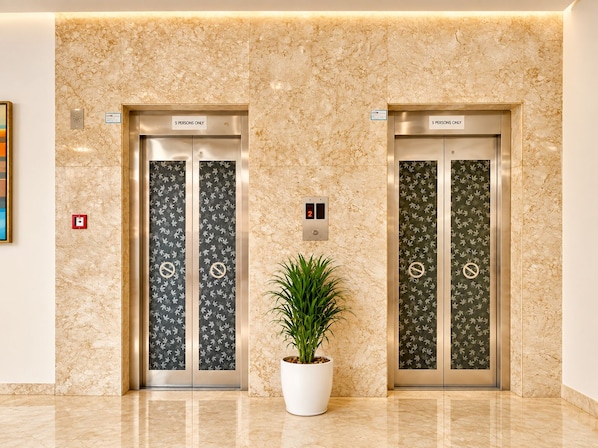 Two elevators with '5 PERSONS ONLY' signs, a potted plant, and a marble wall. - The Altruist Wagholi Hotel (Pune)