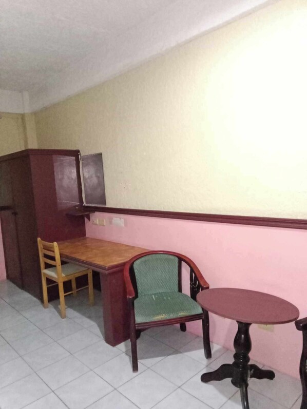 A room with a wooden desk, a green chair, a small round table, and a cabinet.