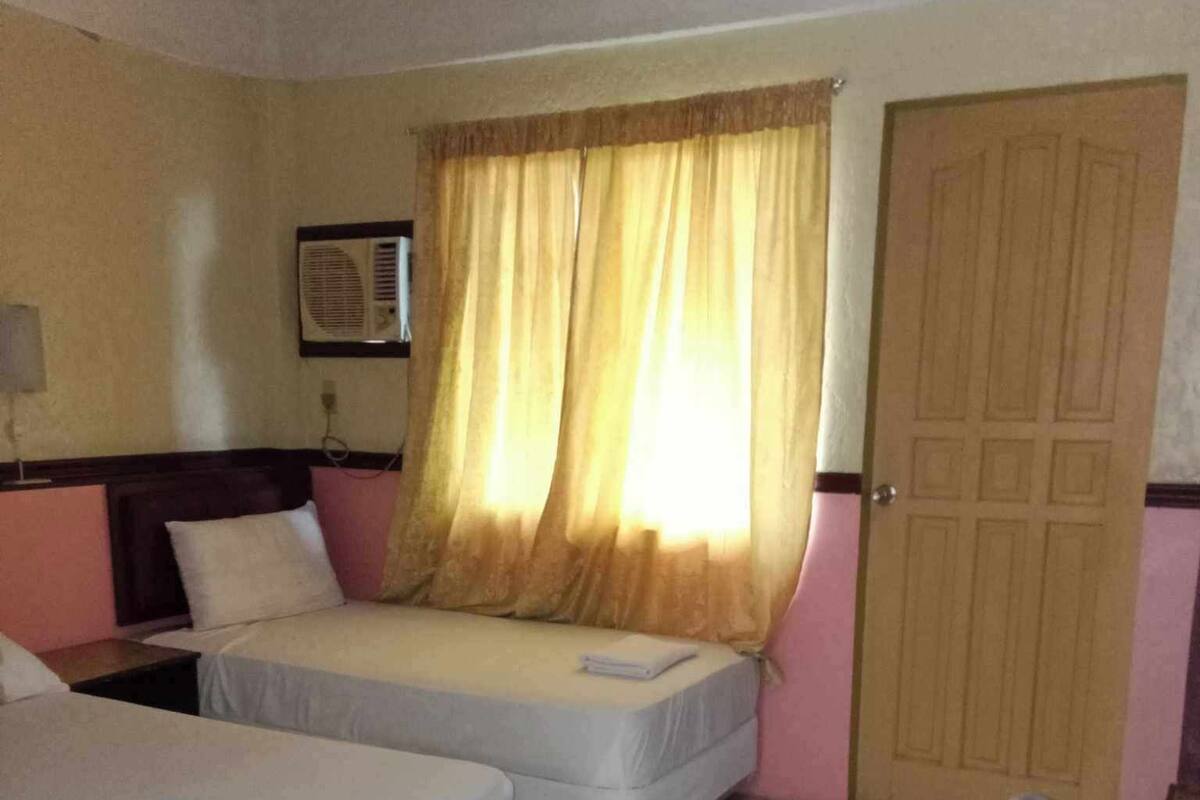A hotel room with two beds, a window with curtains, a door, and a tiled floor.