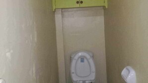 Une petite salle de bain avec des toilettes, un meuble vert au-dessus et un lavabo blanc sur la gauche.