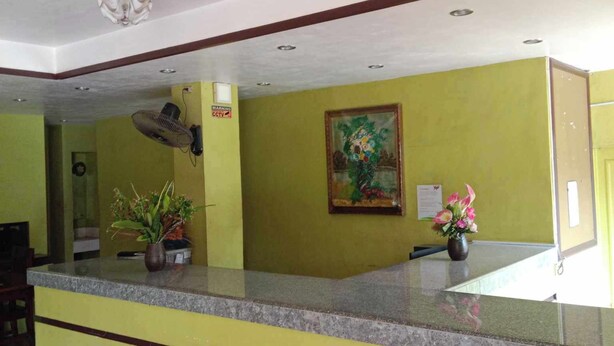Un espace d’accueil avec un comptoir en marbre, des murs verts, un ventilateur de plafond et un tableau.