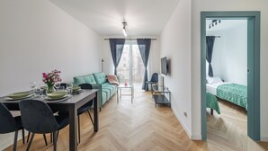 A modern, well-lit room with a dining area, a sofa, a TV, and a bed.