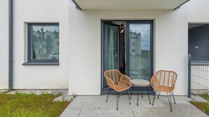A balcony with two wicker chairs and a small table, a sliding glass door, and a view of buildings in the background.