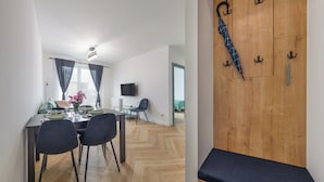 A modern dining area with a table set for two, a TV mounted on the wall, and a wooden door with hooks.