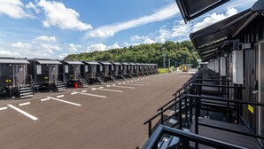 A row of identical cabins with steps leading up to the entrance, a parking lot, and a forested hill in the background. - HOTEL R9 The Yard Usa (Usa)