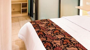 Habitación de hotel con cama, armario con puerta de espejo, un pequeño rincón de descanso y baño visible a través de una puerta abierta.