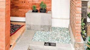 Un pequeño espacio al aire libre con un muro de ladrillo, una puerta blanca y un jardín con plantas en macetas.